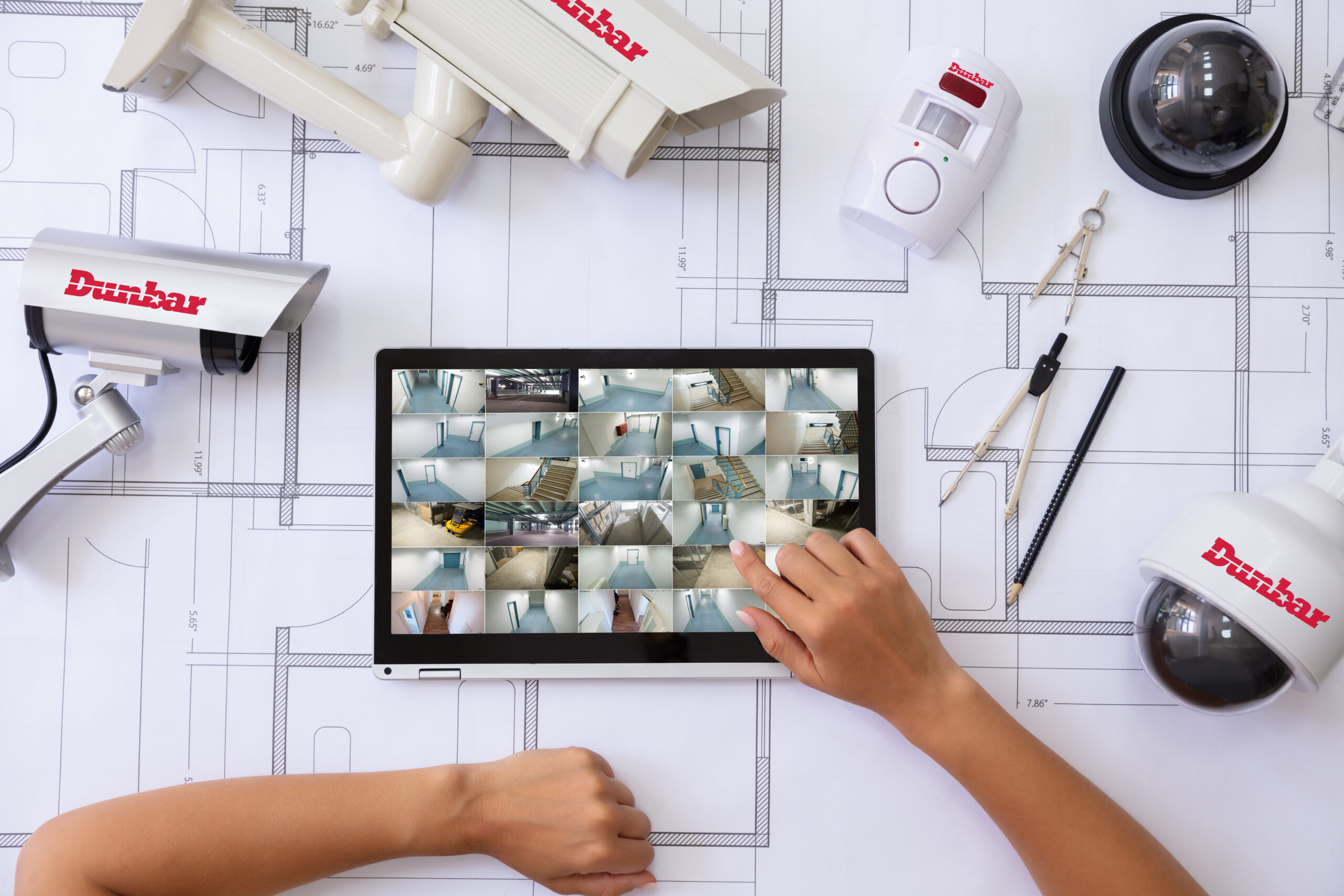 Watching Footage On Laptop With Security Equipment On Blueprint